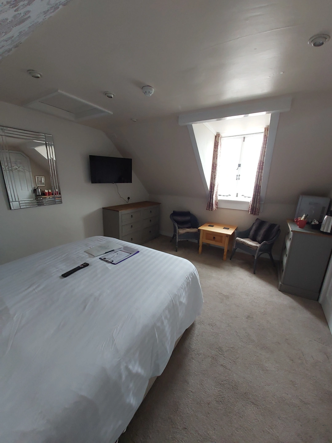 Bright guest bedroom with double bed, seating, television and window.
