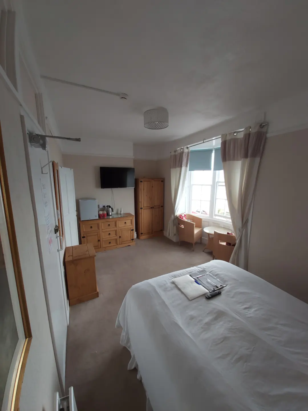 Bright guest bedroom with wooden furniture, television, seating and windows.
