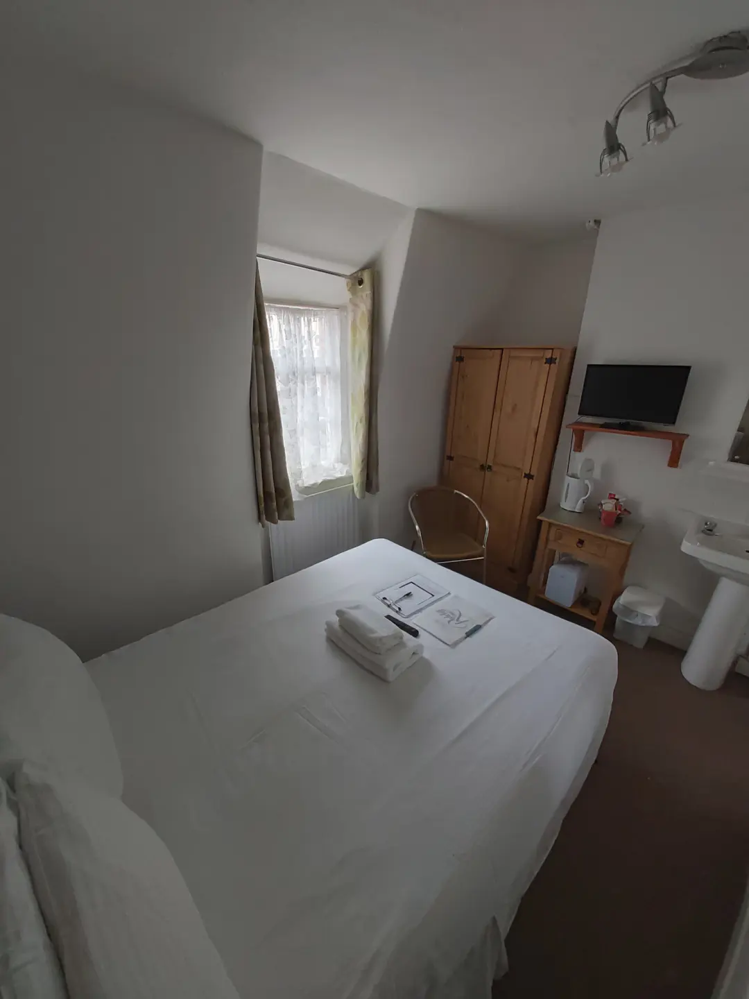 Bright guest room with double bed, television, wardrobe and sink.