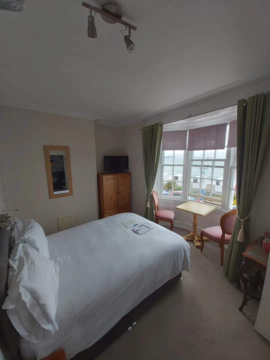Bright, comfortable guest bedroom with television, dresser and natural light.