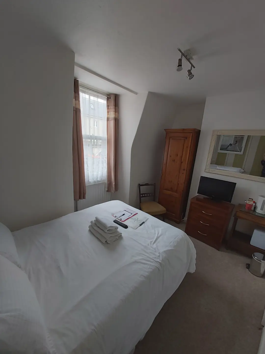 Bright guest bedroom with double bed, wardrobe, television and window.