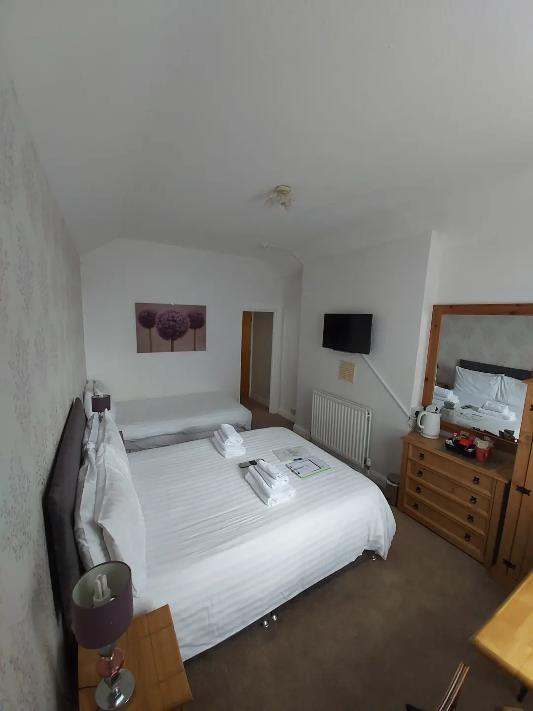 Bright guest bedroom with double bed, television, mirror and furnishings.